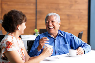 Two seniors enjoying conversation and coffee in a communal dining area.