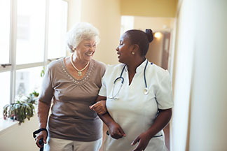 Smiling senior woman walking with a nurse in a bright hallway.