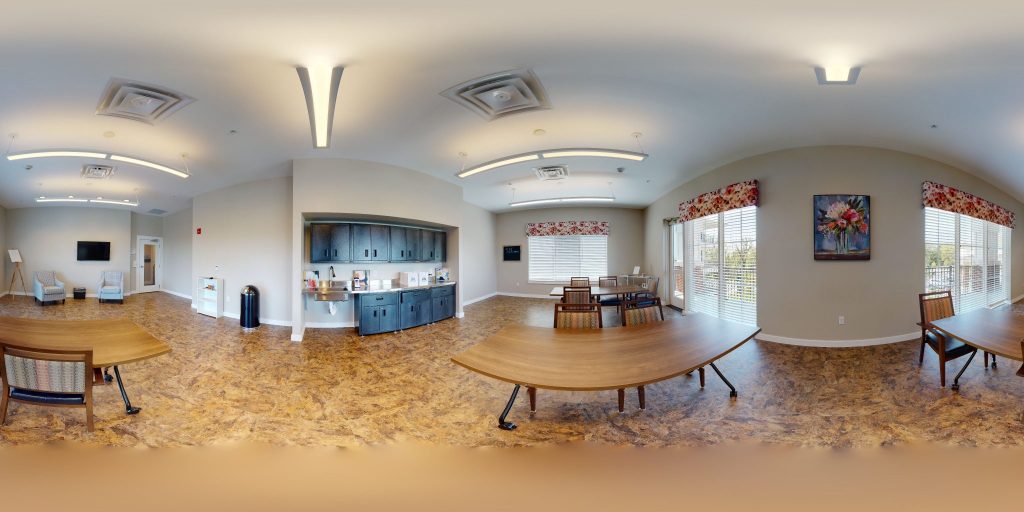 Spacious common room with seating, dining tables, and a kitchenette in a residential building.