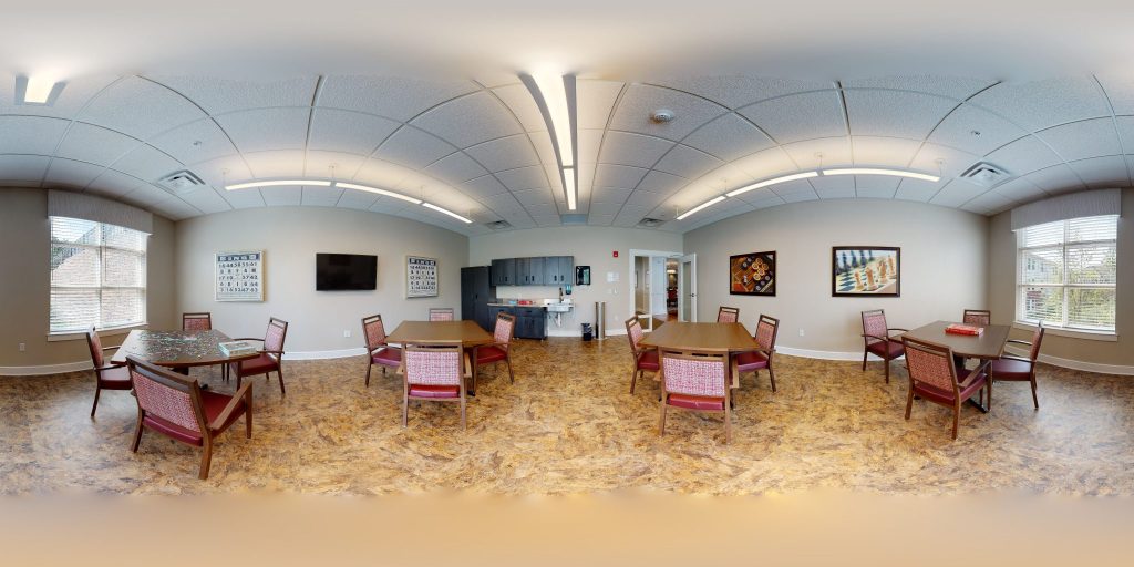 Spacious activity room with tables, chairs, and wall art under soft lighting.
