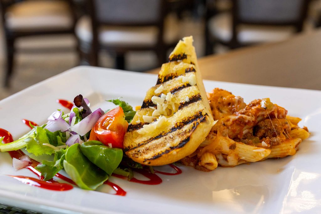 Grilled garlic bread, pasta in tomato sauce, and fresh salad on a white plate.
