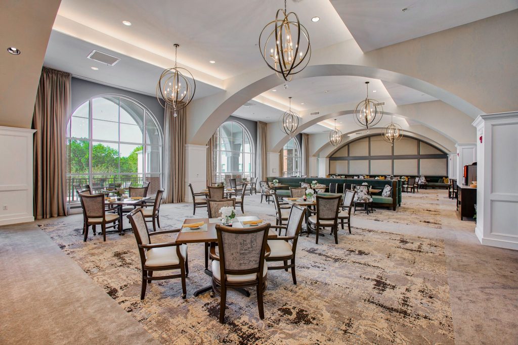 Spacious dining area with large windows and elegant chandeliers at a residential community.