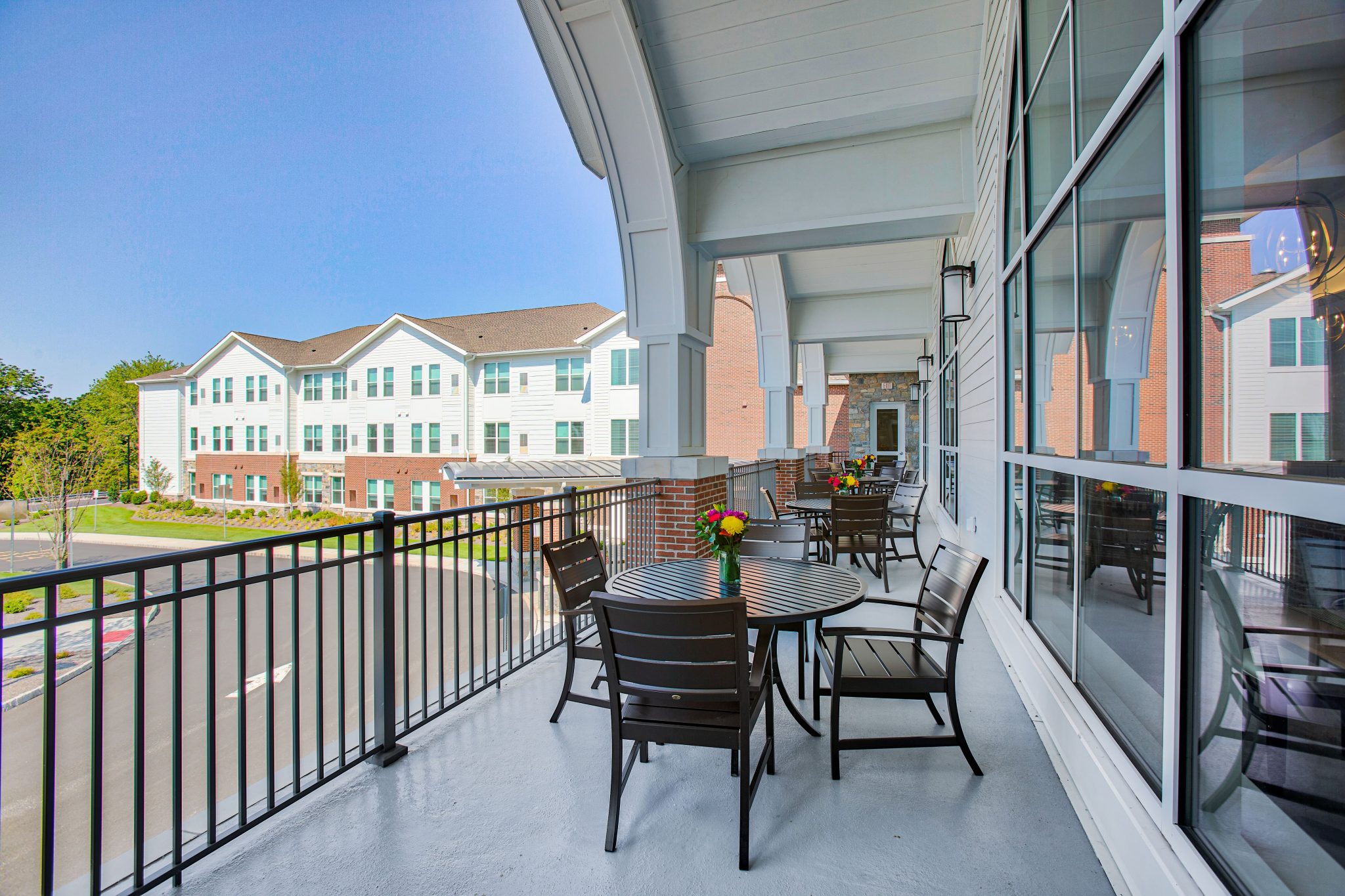 Spacious outdoor balcony with round tables and chairs overlooking row of residential units.